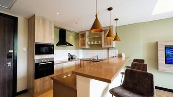 A modern kitchen with a central island, built-in appliances, pendant lighting, and a flat-screen TV mounted on the wall.
