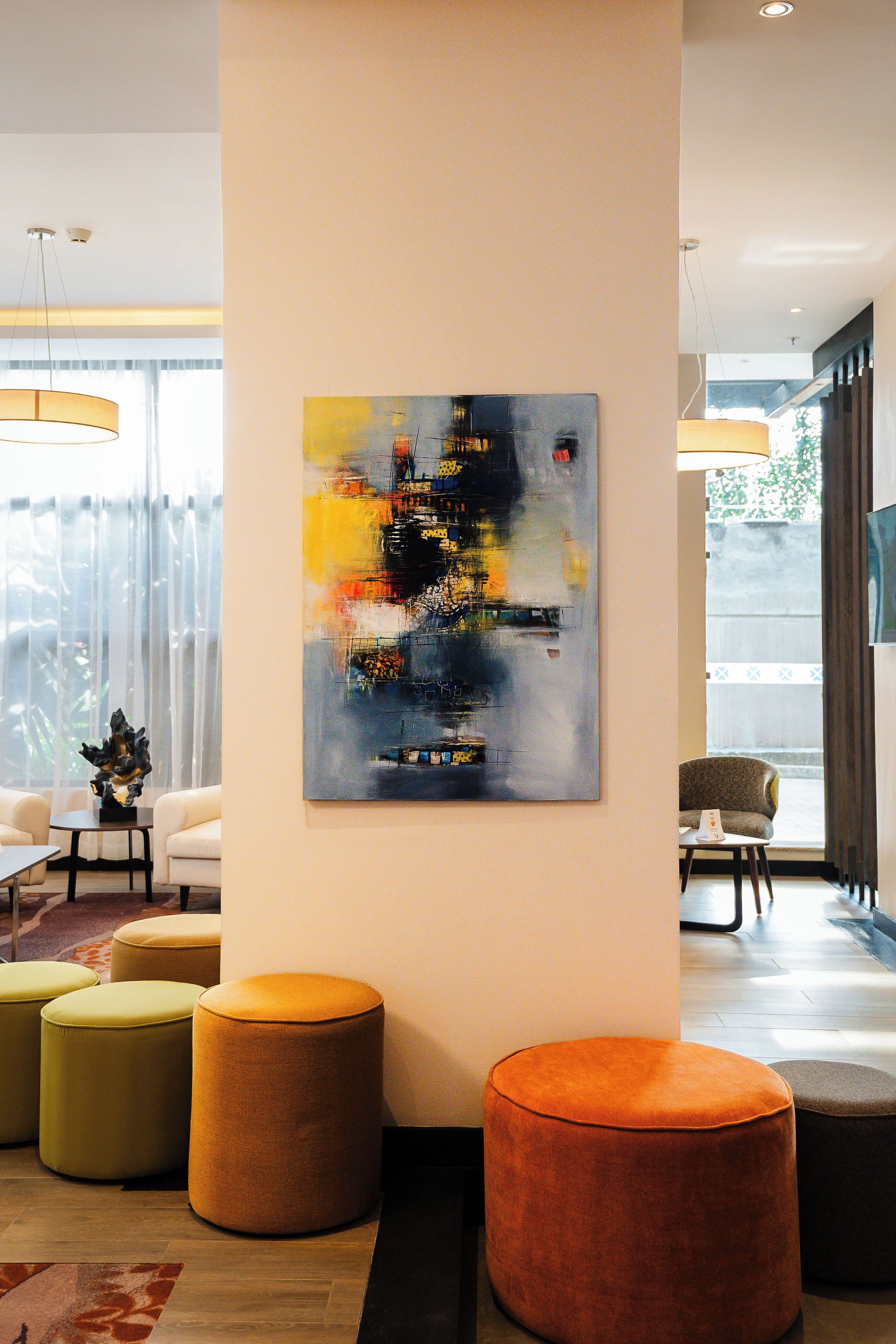 A modern interior with a large abstract painting, multiple round ottomans, and a seating area with a view of the outdoors.