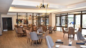 Un espace repas moderne avec un plancher en bois, des meubles contemporains et de grandes fenêtres offrant une vue sur l’extérieur.