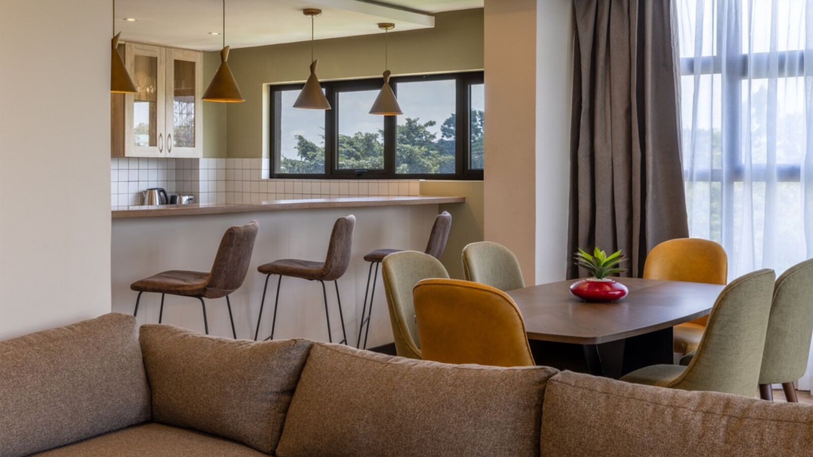 A modern kitchen with a dining area, featuring a sofa, chairs, and a table with a red bowl.