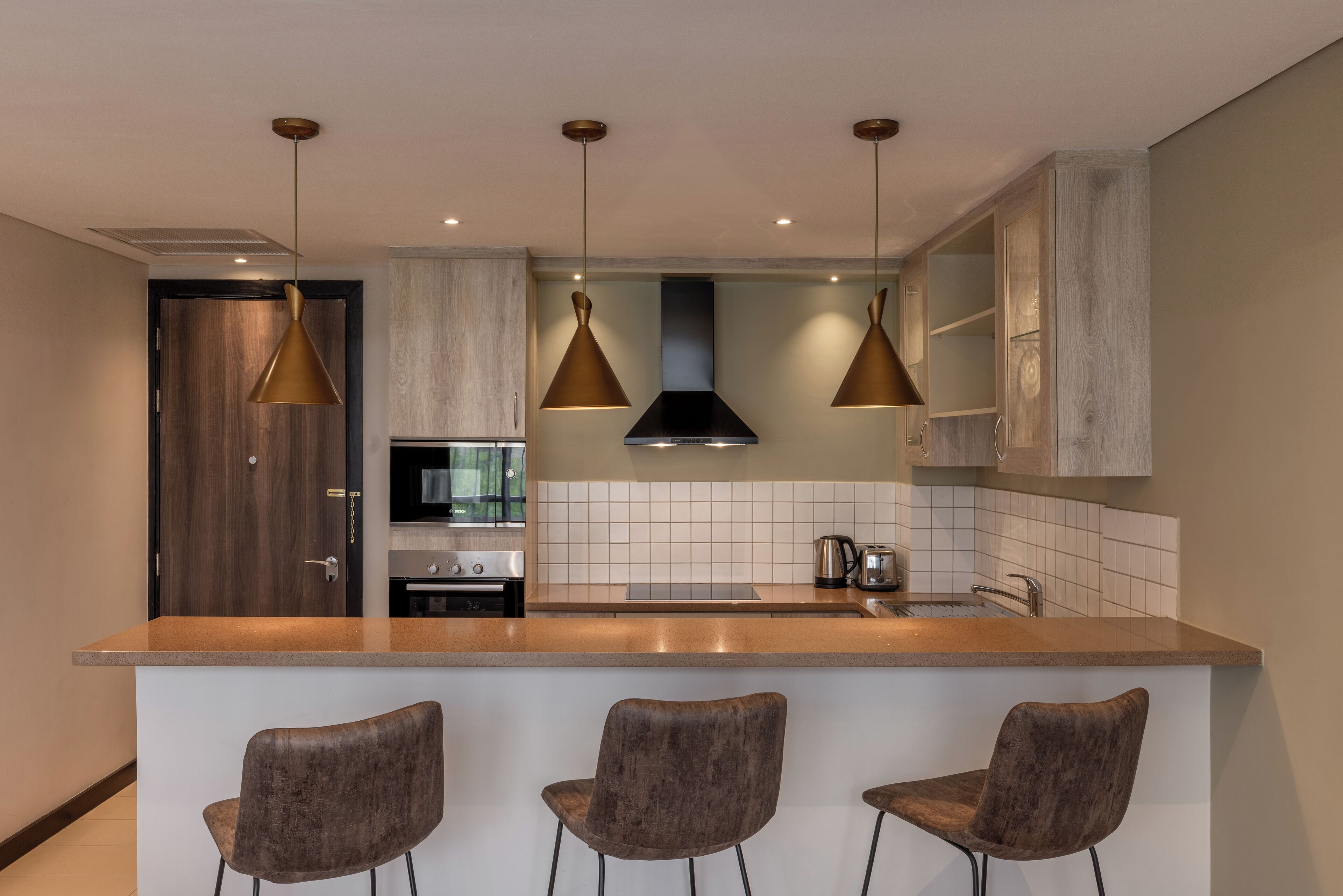 Une cuisine moderne dotée d’un îlot central, de luminaires suspendus et de tabourets de bar.