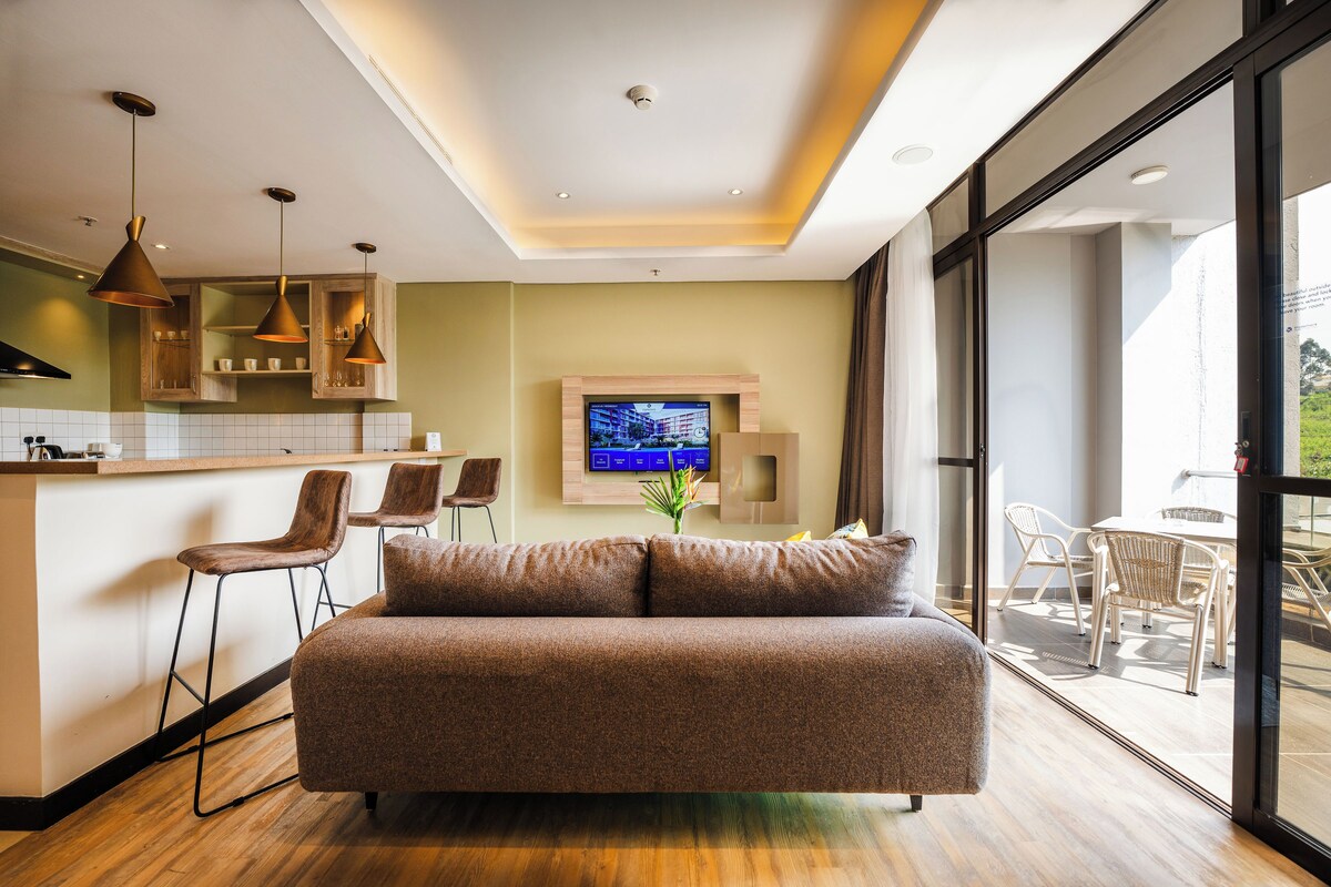 A modern kitchen with a central island, a dining area with a table and chairs, and a living area with a sofa and a TV.