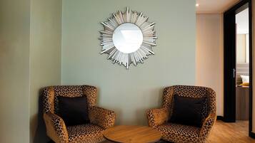 A room with two giraffe-patterned chairs around a round wooden table, a wall-mounted mirror, and a wooden floor.