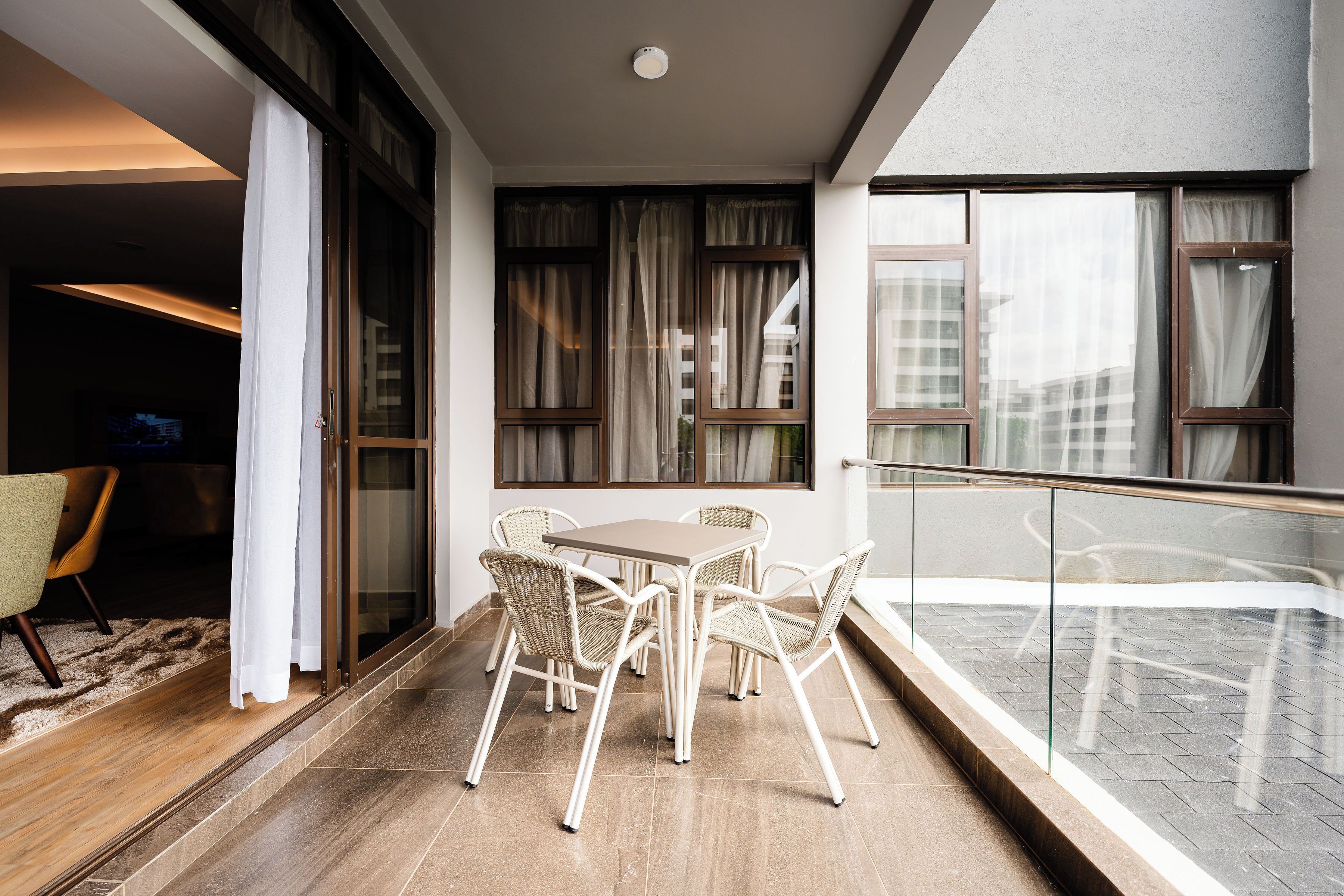 A balcony with a glass railing, a dining table with four chairs, and a view of the cityscape.