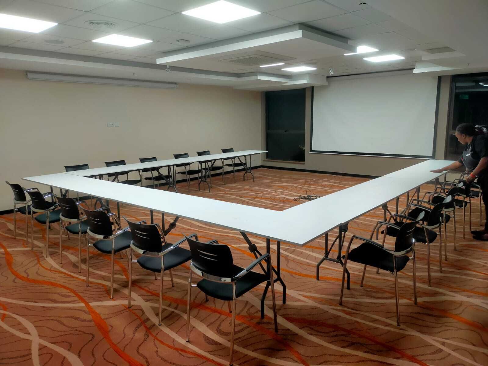 Une salle de conférence avec une longue table et des chaises, un écran de projection et un sol recouvert de moquette.