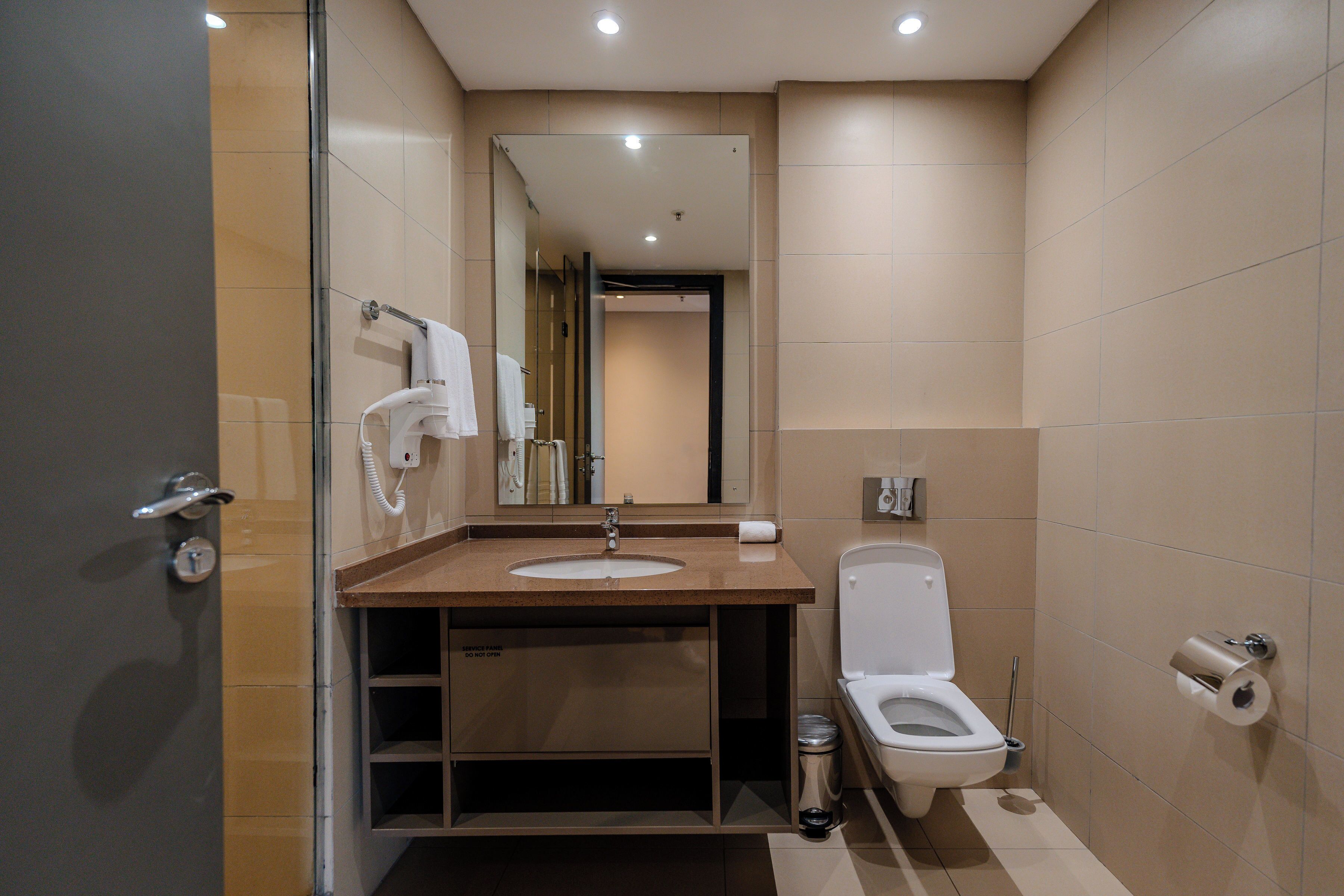 Et moderne badeværelse med et glasbadeværelseskabine, vask med spejl, toilet og skraldespand.