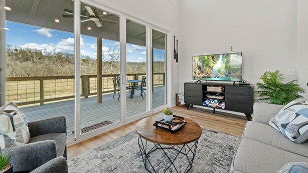A spacious living room with a large TV, comfortable seating, and a view of the outdoors. - War Eagle Creek Retreat- Cabin on the Creek- Private but close to everything (HUNTSVILLE)