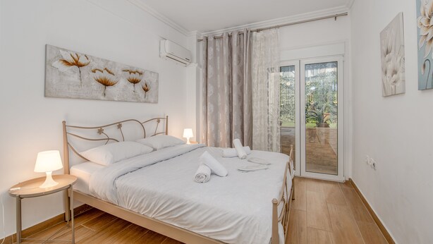 A bedroom with a bed, bedside lamps, a window with curtains, and artwork on the walls. - Kalithea Gardenspot (Kallithea)