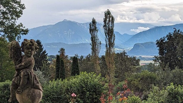 Ein Garten mit einer Steinstatue, üppigem Grün und einer Bergkulisse.