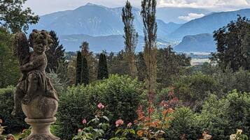 Ein Garten mit einer Steinstatue, üppigem Grün und einer Bergkulisse.