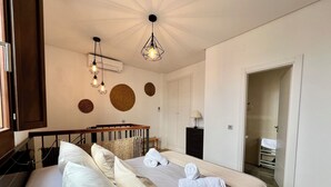 Ein Schlafzimmer mit zwei Betten, einem Holz-Kopfteil, einer Deckenleuchte, einer wandmontierten Klimaanlage und einer Tür zu einem anderen Raum.