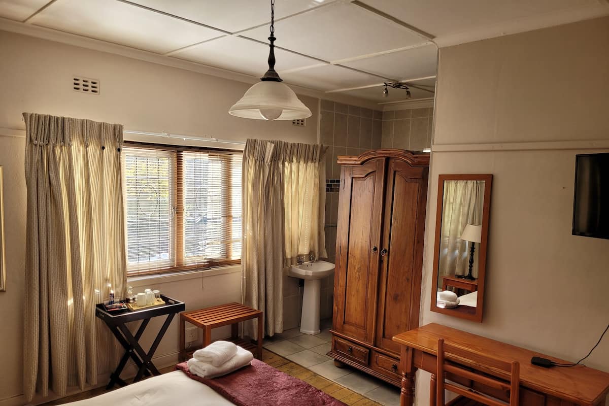 Habitación de hotel con cama, escritorio, armario, espejo y ventana con cortinas.