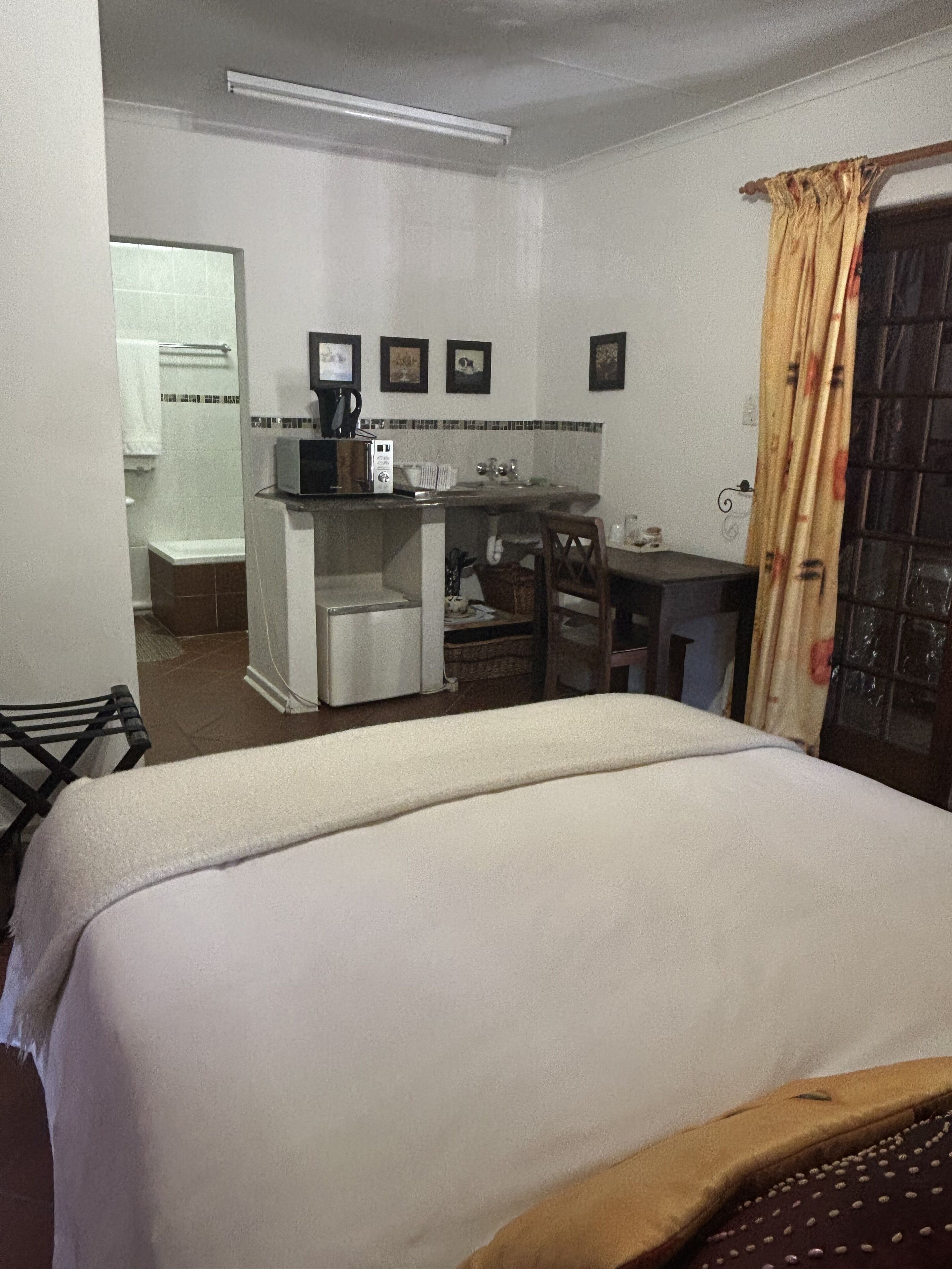 A hotel room with a bed, a desk with a computer, a small kitchenette, and a bathroom visible through an open door.