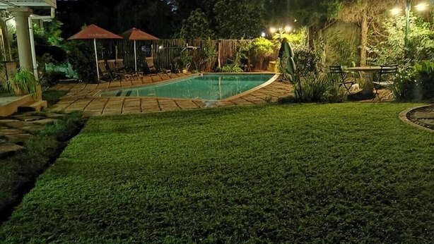 Un patio trasero con piscina, un área de estar techada y un césped bien cuidado.