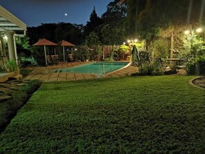 Un jardin avec une piscine, un espace salon couvert et une pelouse bien entretenue.