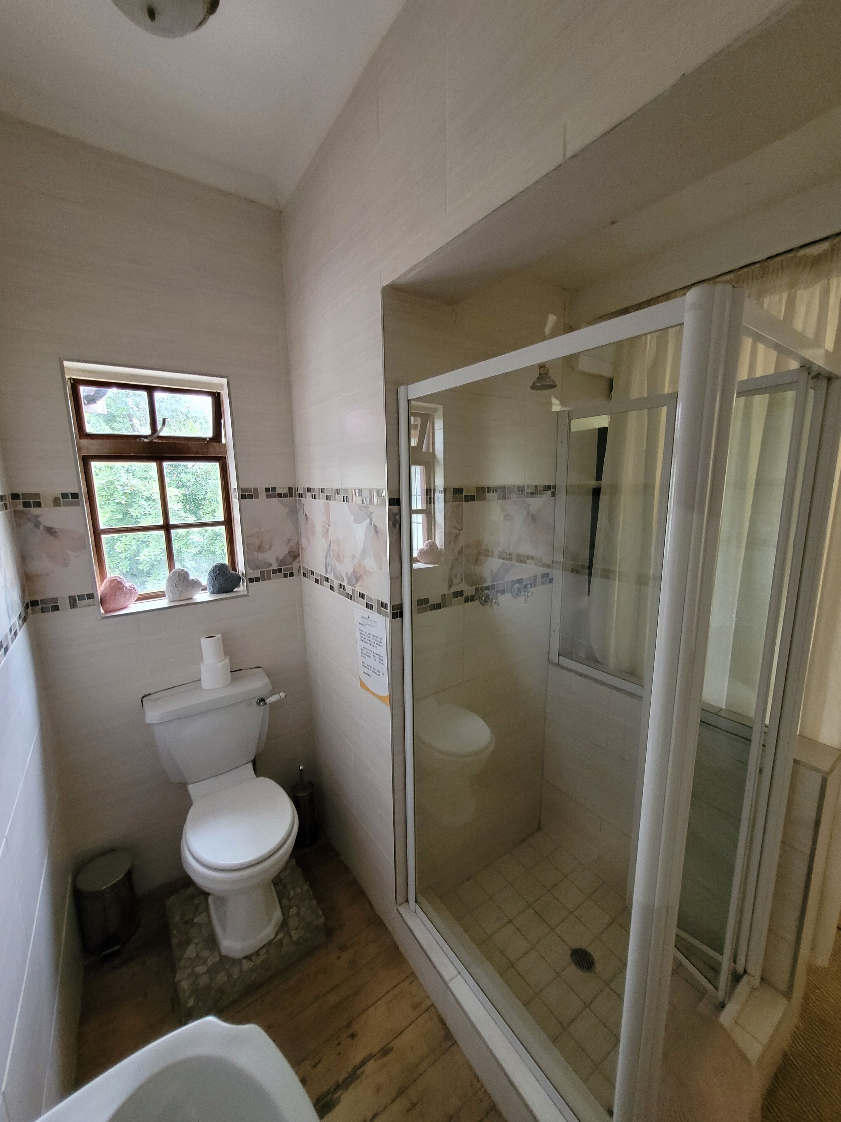 Un baño con inodoro, ventana y zona de ducha con mampara de cristal.