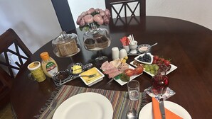 Una mesa de comedor dispuesta con platos, cubiertos, un vaso de agua y diversos alimentos, entre ellos pasteles, frutas y salsas.