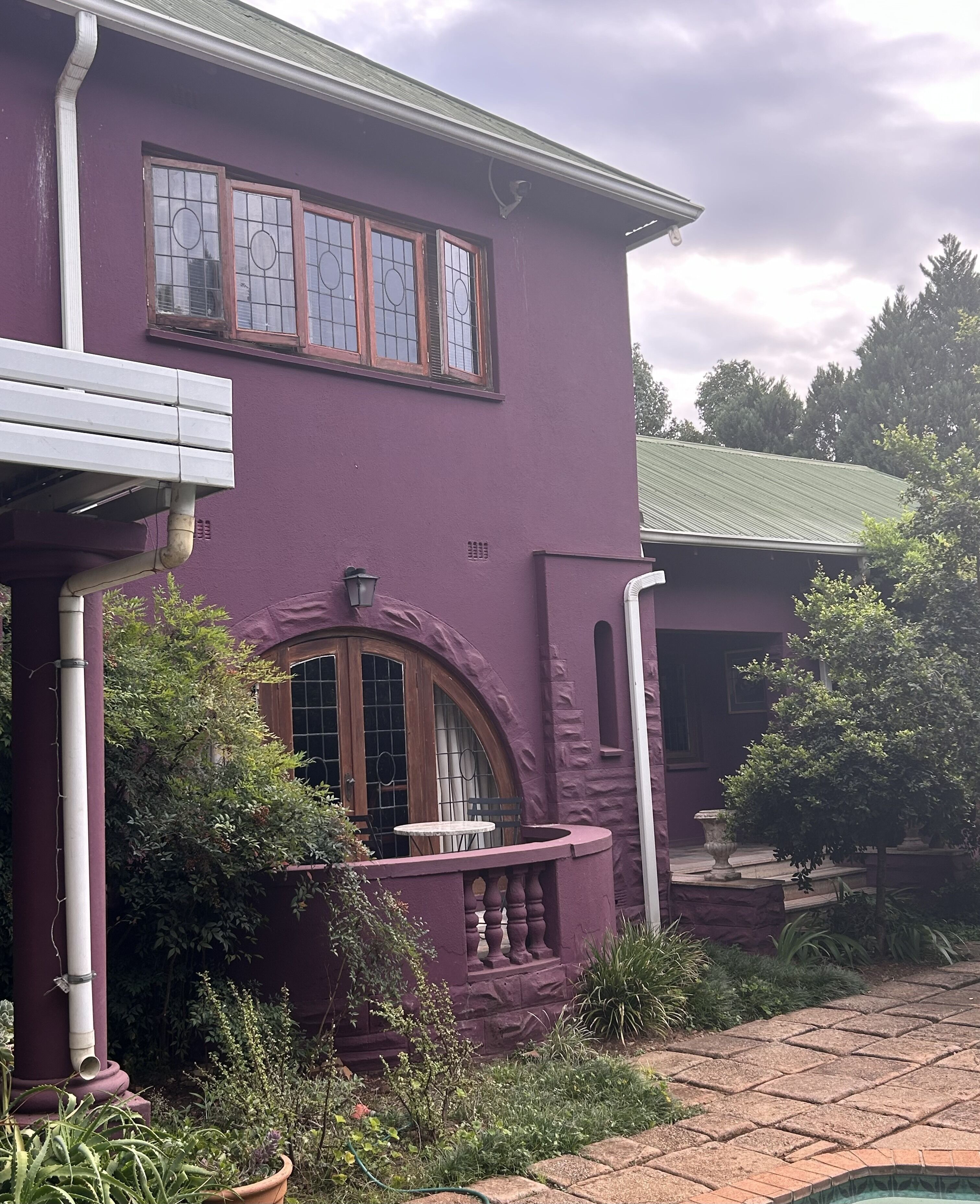 A purple house with a stone facade, a wooden door, and a small round table with chairs outside.
