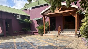 Un edificio con fachada morada, un patio empedrado de piedra y un porche de madera.