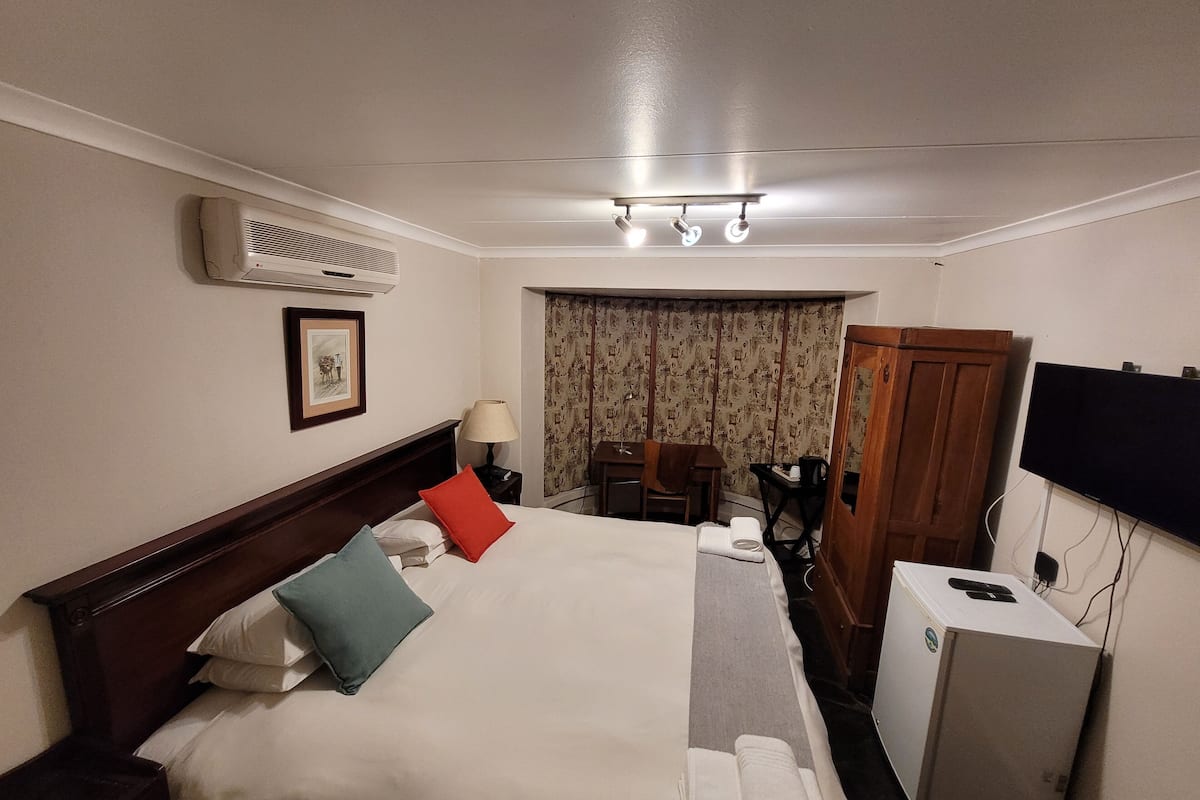 Habitación de hotel con cama, escritorio, silla, armario y televisor.