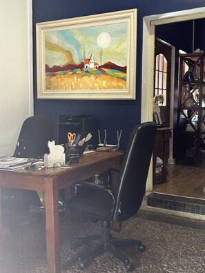 A home office with a desk, computer, and a painting of a landscape with a house and moon.