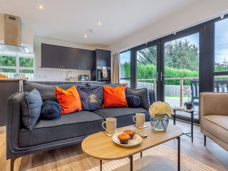 A modern living room with a sofa, a coffee table with muffins, and a view of the kitchen and outdoor deck.