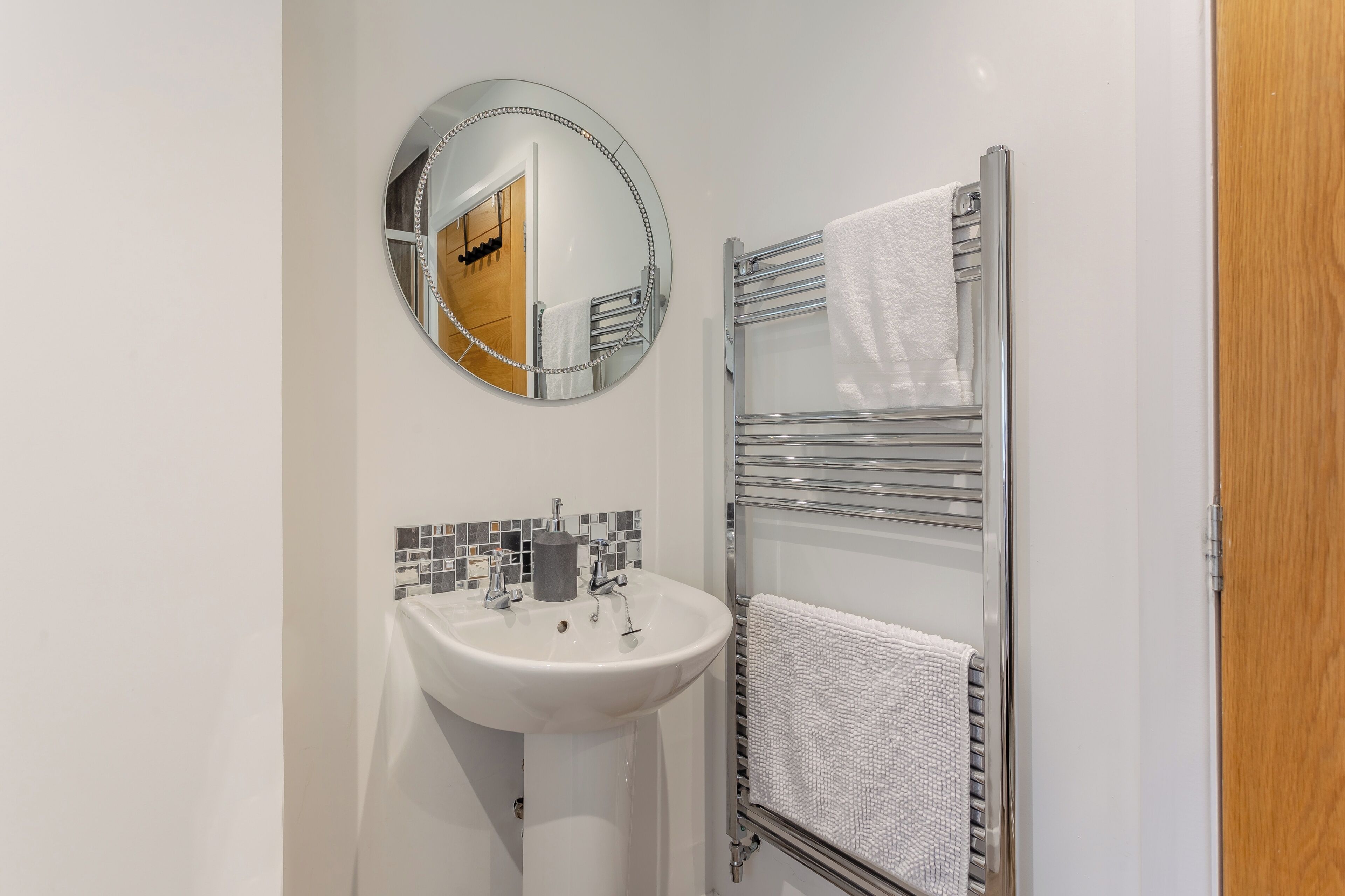Een badkamer met een witte wastafel, een ronde spiegel, een handdoekhouder en een douchecabine met glazen wanden.