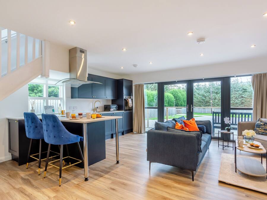 A modern kitchen with dark cabinets, a central island, and a dining area with a sofa and coffee table.