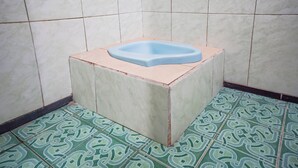 A small, square bathroom with a blue toilet, tiled walls, and patterned floor tiles. - Hotel O Wunut Homestay Syariah (Sidoarjo)