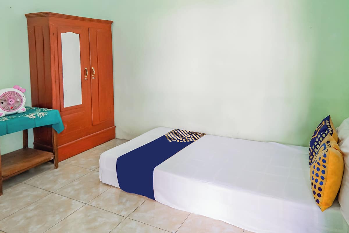 Ein Zimmer mit einem Bett, einem Holzschrank, einem kleinen Tisch mit Tischdecke und einem dekorativen Gegenstand.