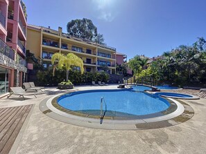A pool area with multiple swimming pools, lounge chairs, and a multi-story building with balconies. - The View by Atlantic Holiday (Funchal)