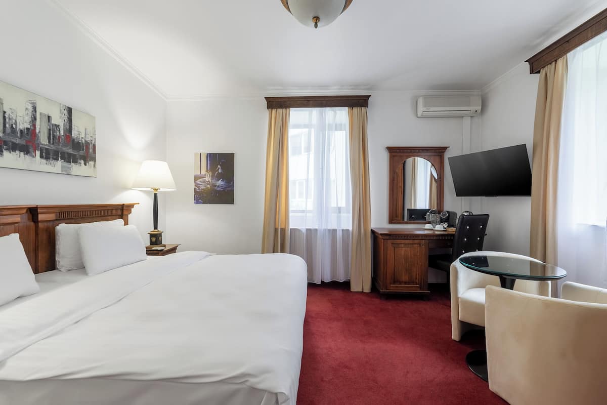 Una habitación de hotel con una cama grande, un escritorio con silla, un televisor y una ventana con cortinas.