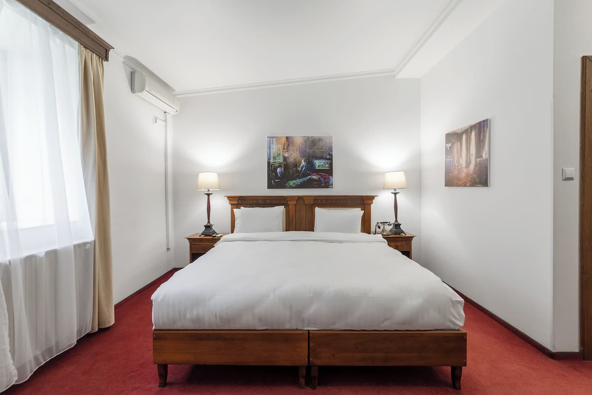 Una habitación de hotel con una cama de madera, ropa de cama blanca, dos lámparas de noche y un cuadro en la pared.
