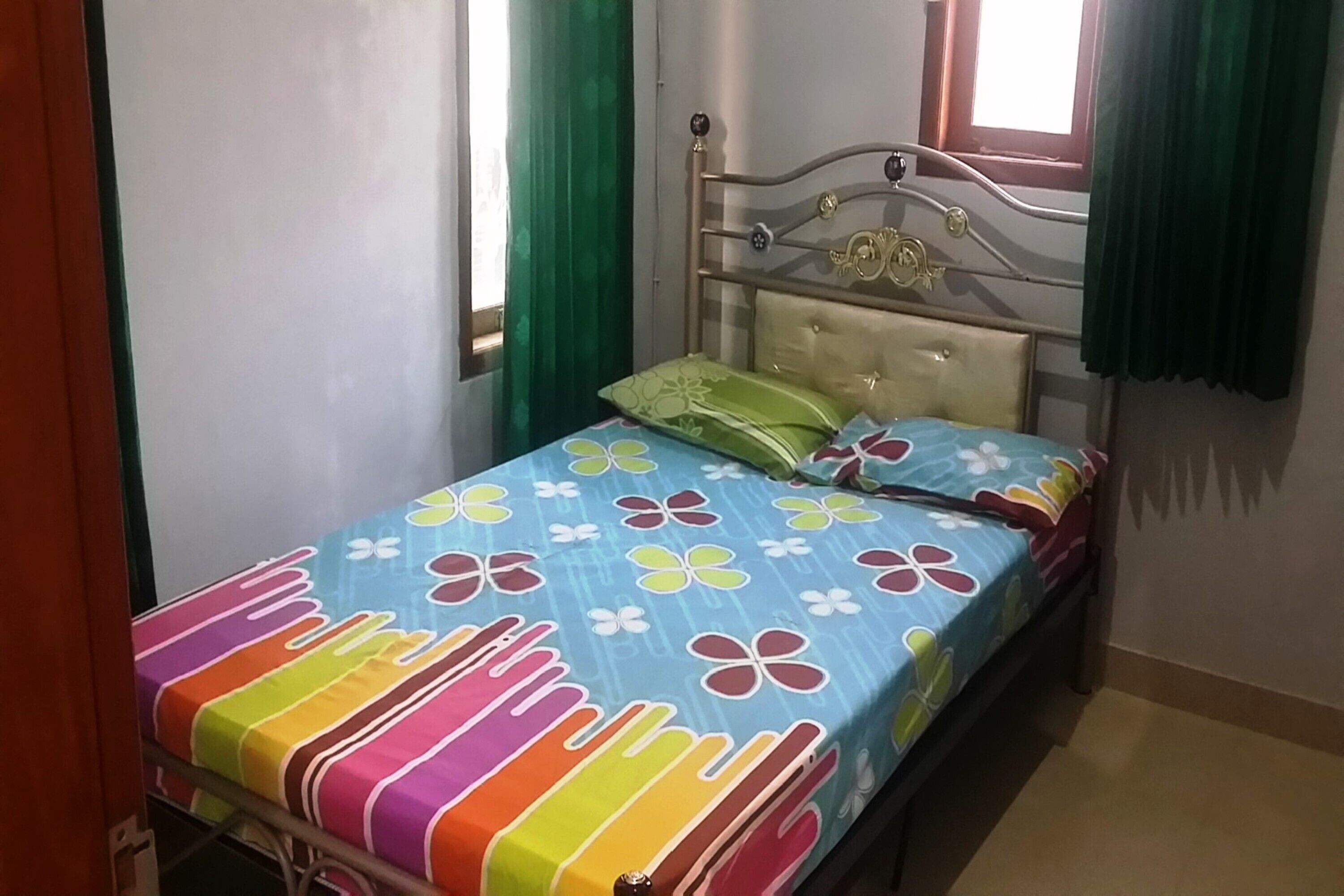 A bed with a colorful floral bedspread, a metal headboard, and green curtains.
