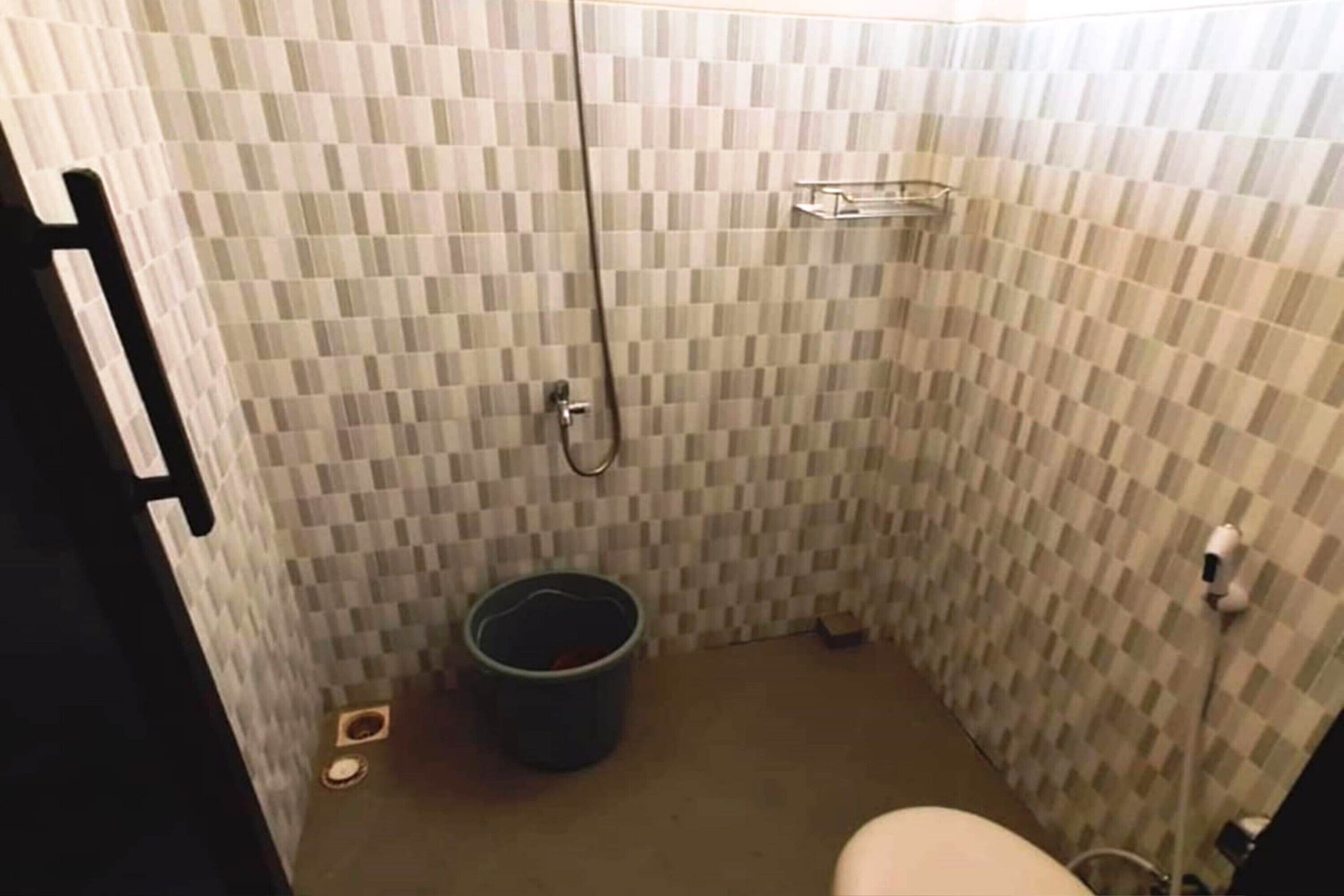 A small bathroom with checkered tile walls, a shower, a toilet, and a trash bin.