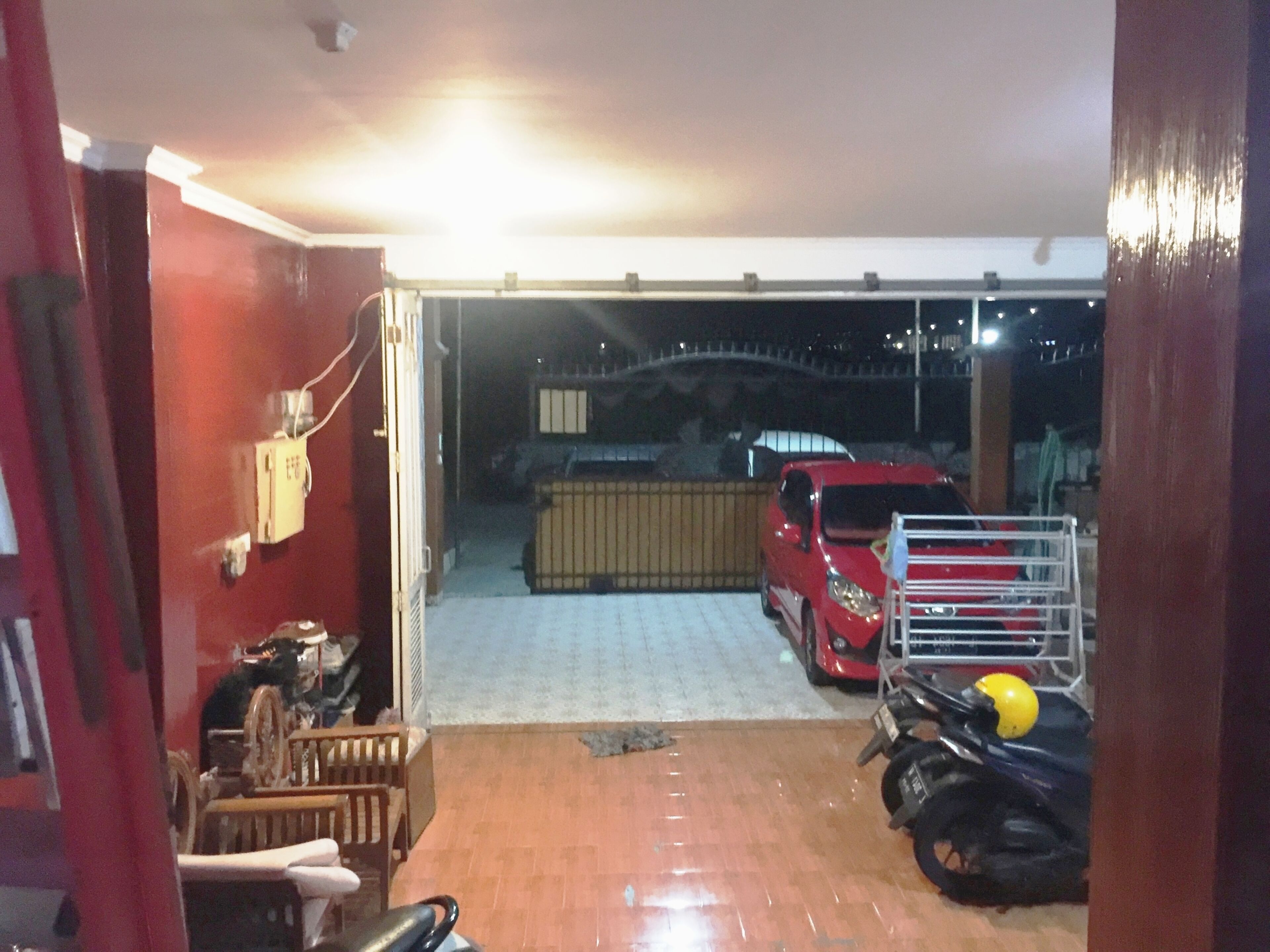 Un garage dans lequel se trouvent une voiture rouge, une moto et un vélo.