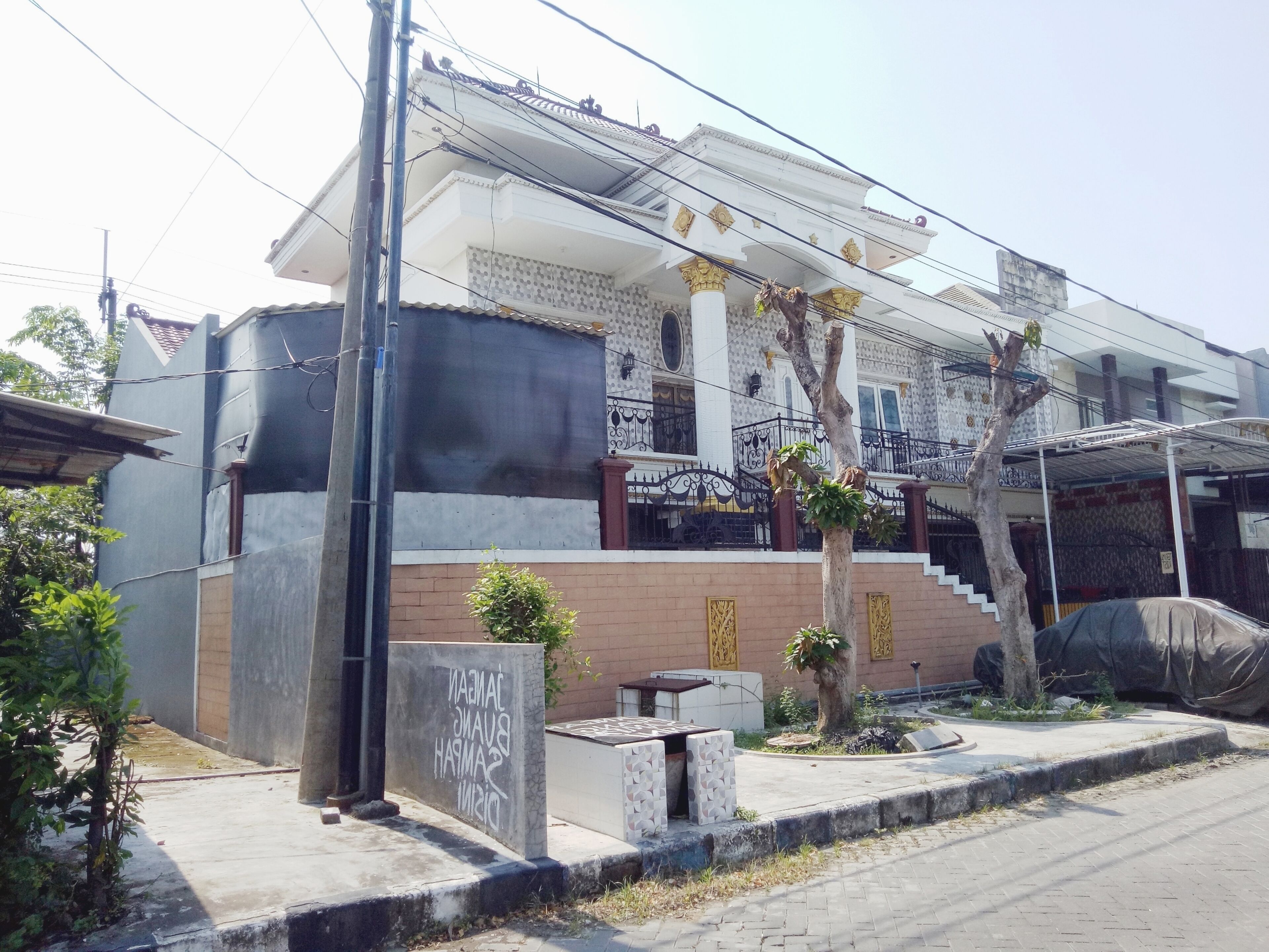 A multi-story building with a balcony, a covered area, and a small garden.