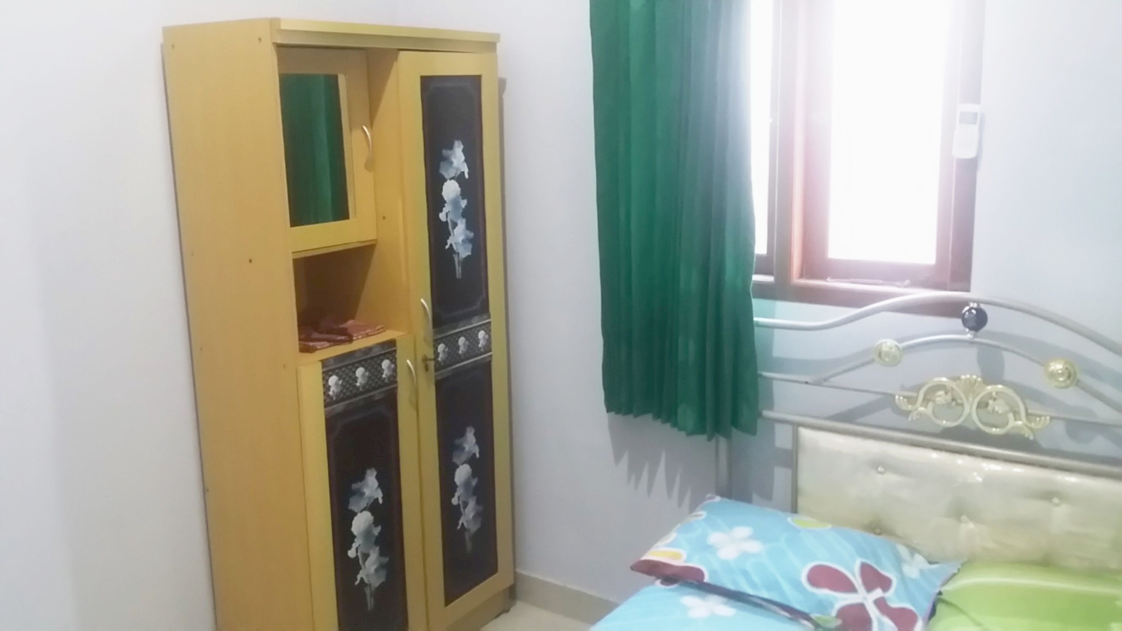 A bedroom with a bed, a wardrobe, and a window with curtains.
