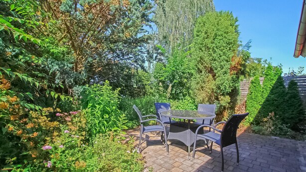 Een terras buiten met een tafel en stoelen, omgeven door weelderige beplanting en bomen.