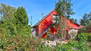 Een rood gebouw met een trap naar een terras, omgeven door groen.