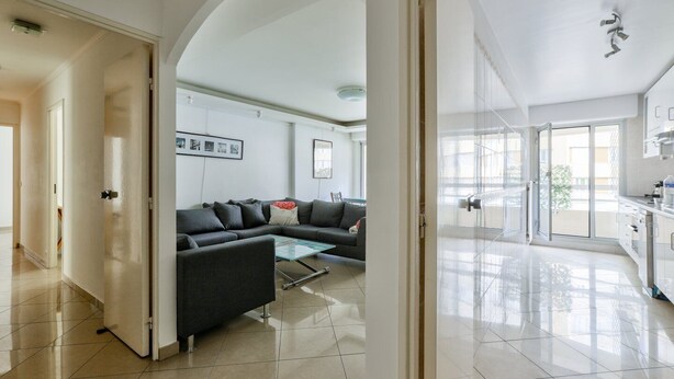 A modern living room with a black sofa, a glass coffee table, and a view of the outside through large sliding glass doors. - Cosy Appart Avec Balcon à Proximité de la Villette (Paris)