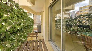 A balcony with a wooden bench, a glass door, and a view of other buildings. - Cosy Appart Avec Balcon à Proximité de la Villette (Paris)