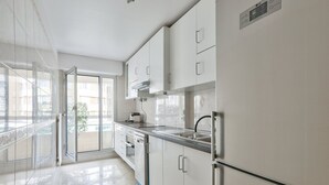 A modern kitchen with white cabinets, stainless steel appliances, and a large window providing natural light. - Cosy Appart Avec Balcon à Proximité de la Villette (Paris)