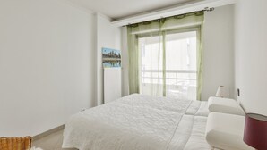 A bedroom with a bed, a chair, a lamp, a window with curtains, and a painting on the wall. - Cosy Appart Avec Balcon à Proximité de la Villette (Paris)