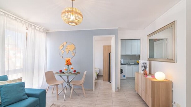 A modern living room with a blue sofa, a dining table with chairs, a globe artwork, and a kitchen in the background. - Vilamoura "charming Algardia" T1 (Quarteira)