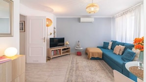 A living room with a blue sofa, a television, a bookshelf, and a decorative lamp. - Vilamoura "charming Algardia" T1 (Quarteira)