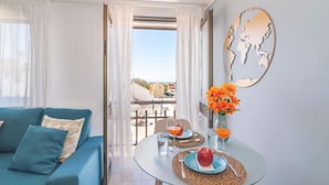 A room with a blue sofa, a glass table with breakfast items, and a view of the outside. - Vilamoura "charming Algardia" T1 (Quarteira)