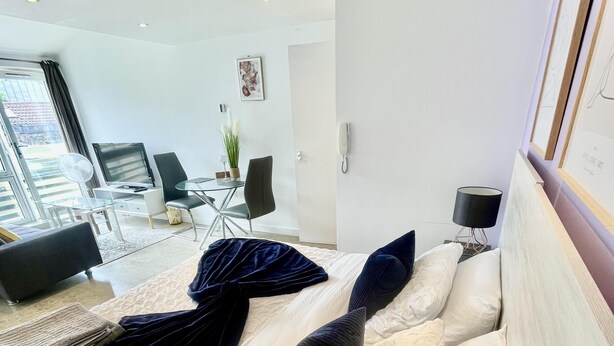 A modern hotel room with a large bed, a desk, a chair, and a dining area visible through a glass door. - Stunning Studio Apartment in Cambridge (Cambridge)