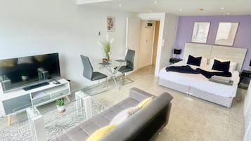 Una sala moderna con televisor de pantalla plana, un sofá, una mesa de comedor con sillas y una cama con cabecera.