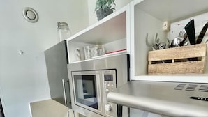 A compact kitchen with a built-in microwave, oven, and toaster. There is a sink with a dish rack, a small plant on the countertop, and a wooden box with utensils. - Stunning Studio Apartment in Cambridge (Cambridge)